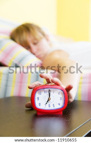 Young woman snoozing a red alarm clock