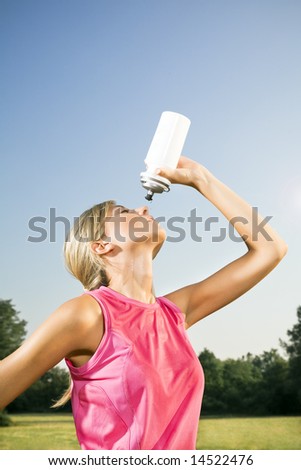Young woman drinking from water bottle outdoors after jogging, copy space