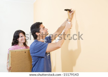 Young Hispanic couple hanging picture on wall