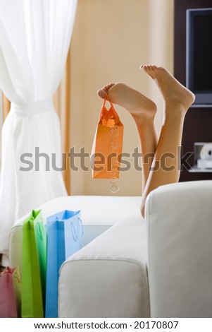 Young woman's legs dangling shopping bag