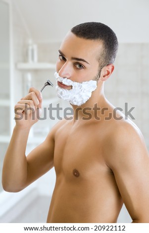 Young man shaving indoors and smiling. Copy space