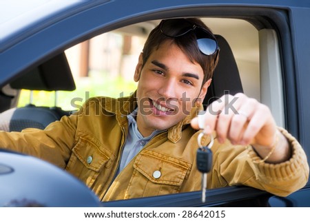 young man sitting inside car showing keys to new car