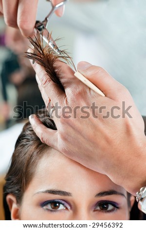 Close up of young woman having her hair being cut. Narrow focus on hand and hair