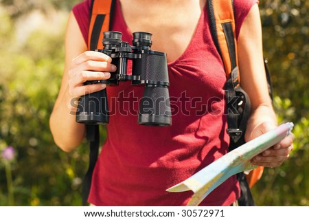 cropped view of female bird watcher holding binoculars and map.