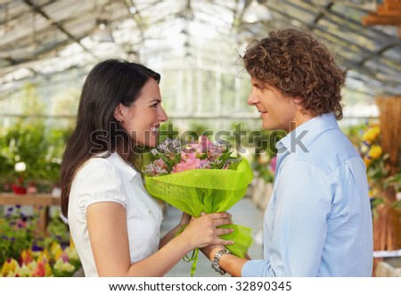 mid adult couple in flower nursery holding bouquet and looking each other