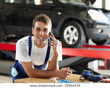 portrait of mechanic talking on mobile phone in auto repair shop. Looking at camera
