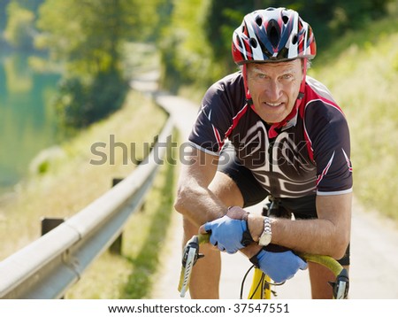senior man leaning on road bike, looking at camera.