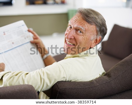 senior man reading newspaper at home and looking over shoulders