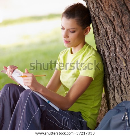 young woman studying outdoors and leaning on tree. Copy space