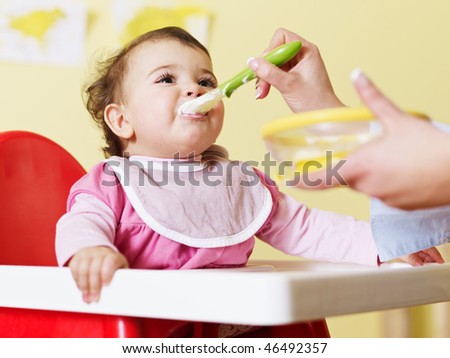 mom giving homogenized food to her daughter on high chair. Horizontal shape