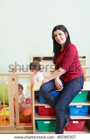 portrait of mid adult teacher in kindergarten. Little girls playing with toys in background. Vertical shape, copy space