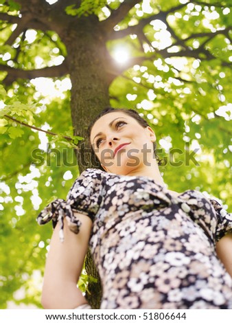 potrait of attractive caucasian woman leaning on tree at sunset and looking away. Low angle view, vertical shape