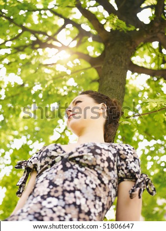 potrait of sad woman leaning on tree at sunset and looking away. Low angle view, vertical shape