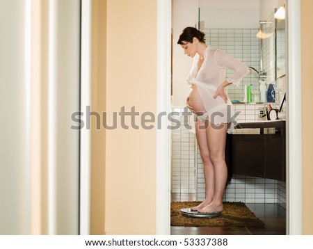 italian 6 months pregnant woman standing on scale in bathroom. Horizontal shape, side view; copy space;
