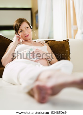 italian 6 months pregnant woman sitting on sofa and listening to her baby heart-rate with electronic stethoscope. Vertical shape, copy space