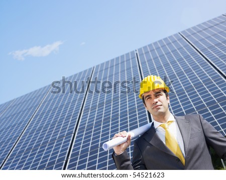 Portrait of mid adult italian male engineer holding blueprints in solar power station and looking up. Horizontal shape, front view. Copy space