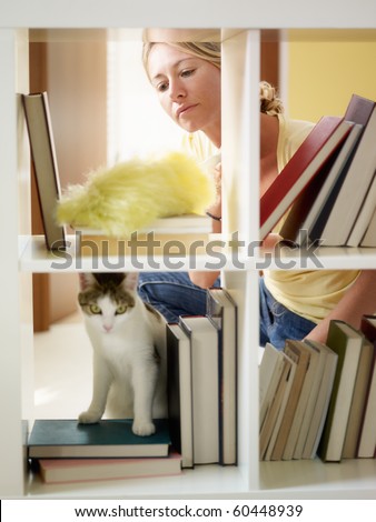 mid adult woman dusting bookshelves. Vertical shape, three quarter length
