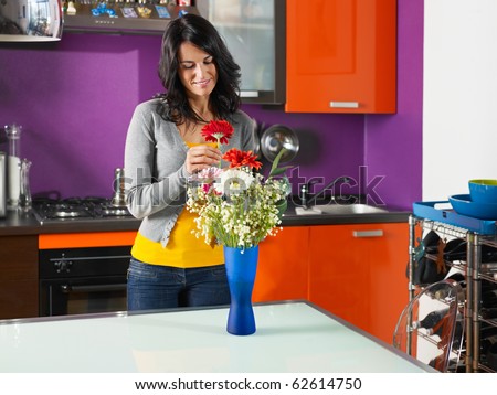mid adult woman putting gerbera in blue pot. Horizontal shape, three quarter length