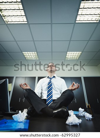 stressed businessman sitting on desk in lotus position. Vertical shape, full length, Copy space