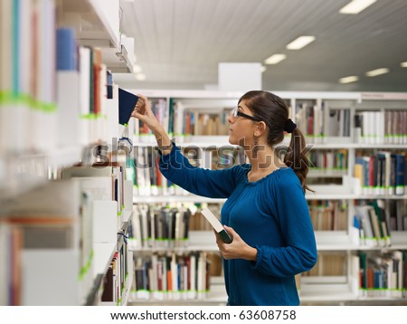 female college student taking book from shelf in library. Horizontal shape, side view, waist up, copy space