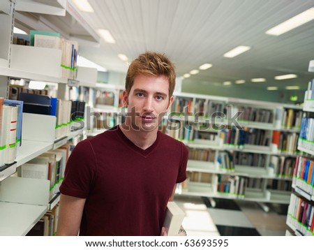 male college student with book standing near shelf in library. Horizontal shape, front view, waist up, copy space