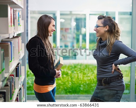 two female college students talking in library. Horizontal shape, side view, waist up