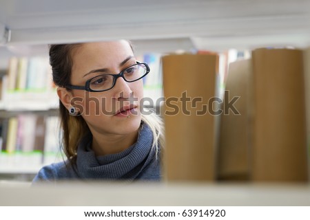 female college student taking book from shelf in library. Horizontal shape, front view, head and shoulders, copy space