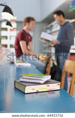 closeup of closed book on table. Two students talking in background. Vertical shape, copy space, focus on foreground
