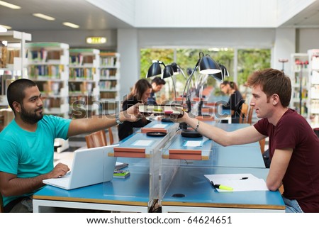 two college students sitting in library with laptop computer and sharing book. Horizontal shape, side view, copy space