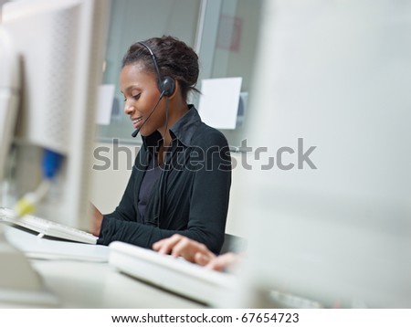 female african american customer service representative talking on the phone and typing on pc. Horizontal shape, side view, copy space