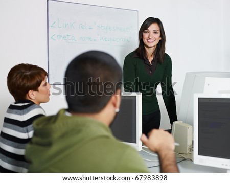 Computer class with caucasian female teacher talking to hispanic student. Horizontal shape, focus on background