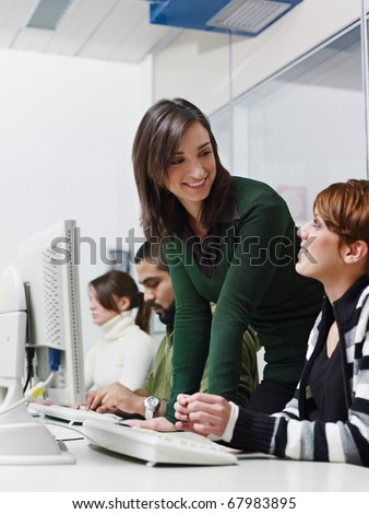 Computer class with caucasian female teacher helping student. Vertical shape, side view, waist up