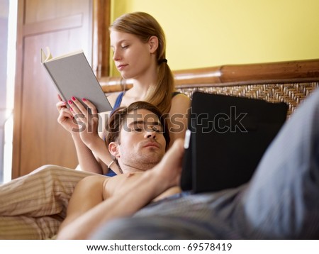 caucasian heterosexual couple having fun on bed with book and tablet pc. Horizontal shape, three quarter length, side view