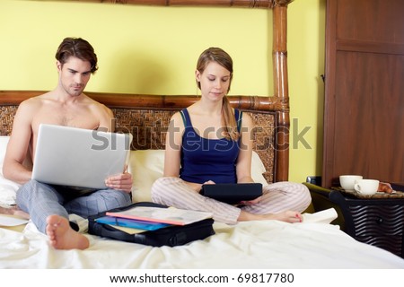 caucasian heterosexual couple working with laptop computer and touch pad in bedroom. Horizontal shape, full length, front view