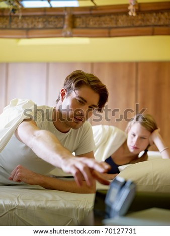caucasian heterosexual couple in bed snoozing alarm clock. Vertical shape, front view, waist up
