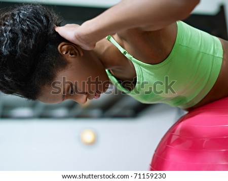 young african american woman in green sportswear exercising back muscles on fit ball in gym. Horizontal shape, side view, copy space