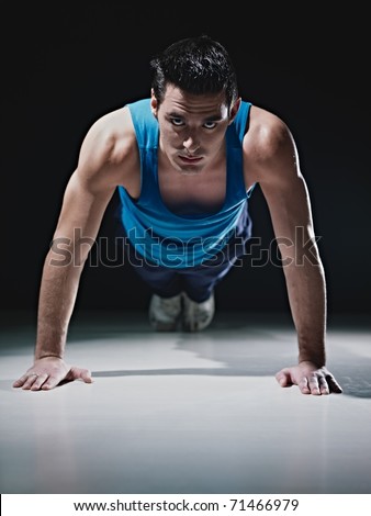 Young caucasian male in sportswear doing push ups on black background. Vertical shape, front view, copy space