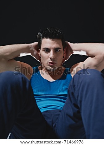 young adult caucasian male in blue sportswear exercising abdominals on black background, looking at camera. Vertical shape, front view, copy space