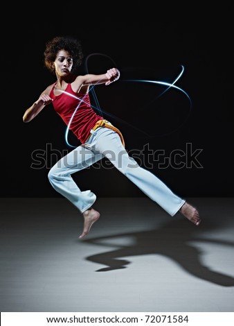 young adult latin american female doing capoeira flying kick in gym, with streaks of led lights all around. Vertical shape, full length, front view, copy space