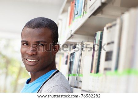 african american male college student leaning on shelf in library and looking at camera. Horizontal shape, head and shoulders, copy space