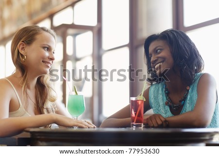 african and latin american female friends drinking cocktails and talking in a pub. Horizontal shape, side view, waist up