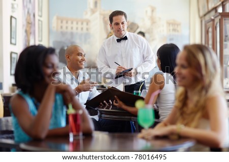 young adult hispanic couple dining out in restaurant and talking to waiter in bow tie. Horizontal shape, front view, waist up