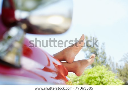 young adult woman relaxing with feet out of convertible red car. Horizontal shape, side view, copy space