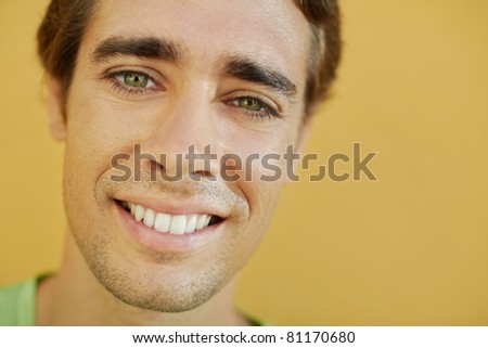 portrait of caucasian college student smiling and looking at camera with yellow wall in background. Selective focus, copy space