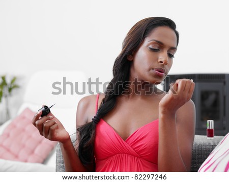Black woman on sofa, applying nail varnish to her fingernails. Horizontal shape, copy space