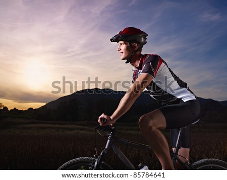 sports activity: young adult cyclist riding mountain bike in the countryside. Horizontal shape, side view, copy space