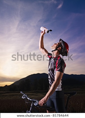 sports activity: young adult cyclist on mountain bike spilling water on face from bottle. Vertical shape, side view, copy space