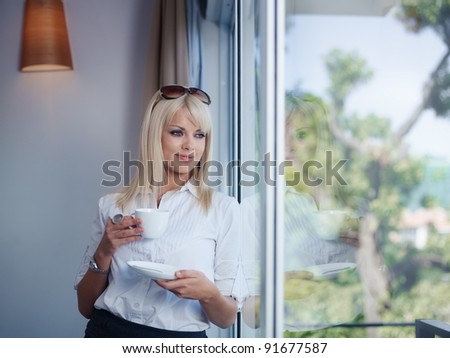 Mid adult businesswoman relaxing and drinking a cup of tea, looking out of window. Waist up, front view, copy space