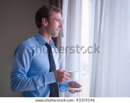 Mid adult business man relaxing and drinking a cup of tea, looking out of window. Side view, copy space