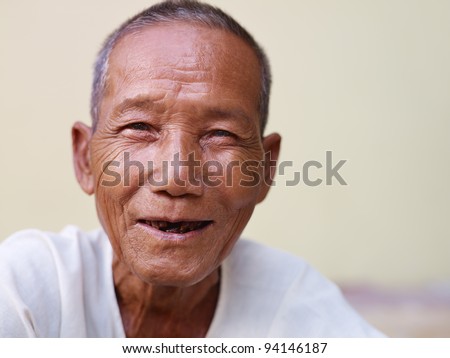 Portrait of happy senior asian man with dental problems laughing and looking at camera against yellow wall